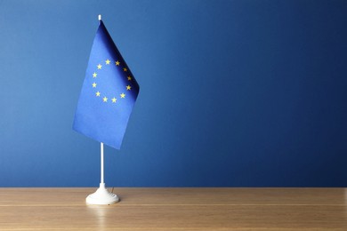 Photo of One flag of European Union on wooden table against blue background. Space for text