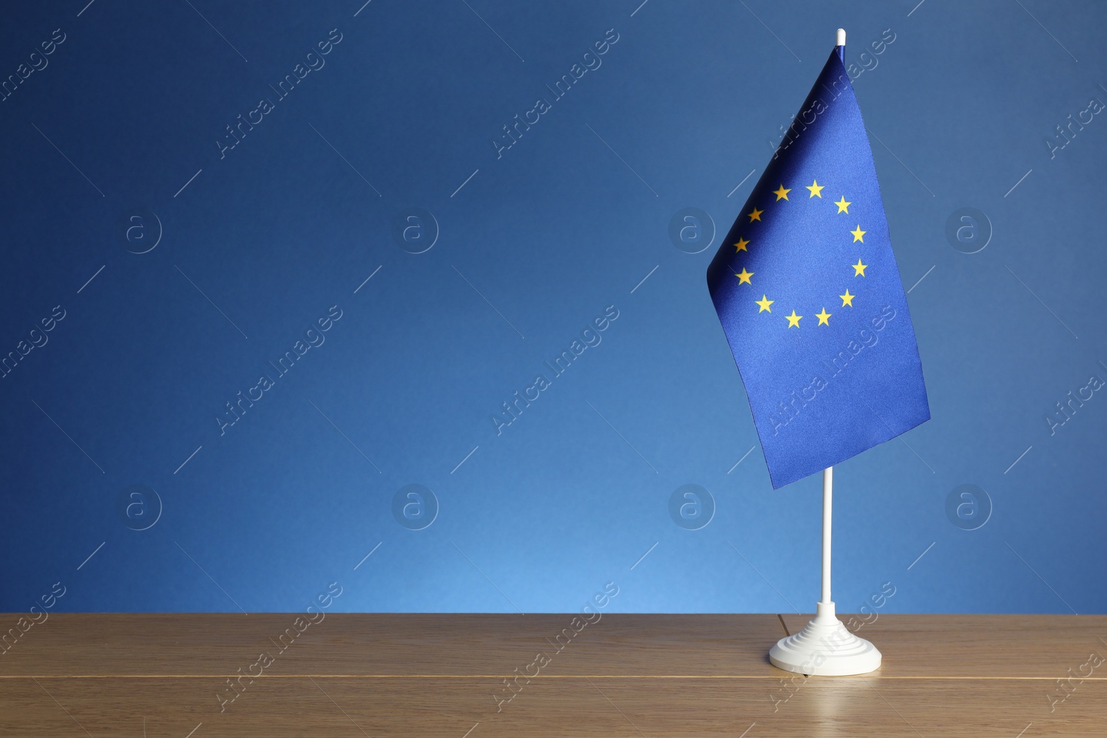 Photo of One flag of European Union on wooden table against blue background. Space for text