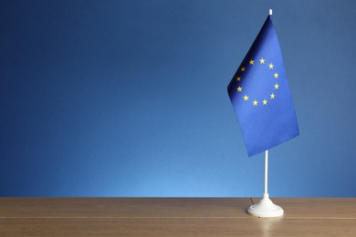 Photo of One flag of European Union on wooden table against blue background. Space for text