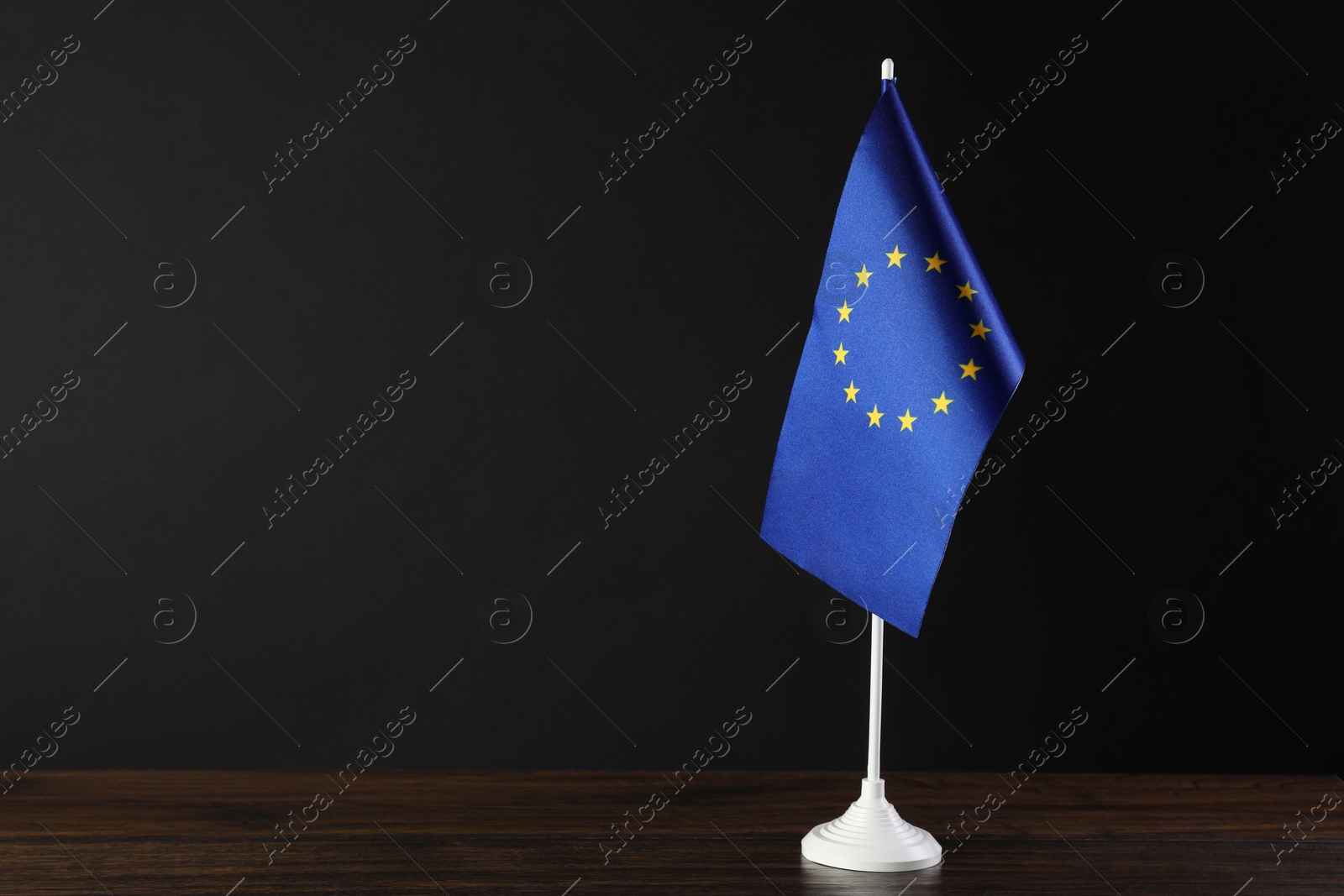 Photo of One flag of European Union on wooden table against black background. Space for text