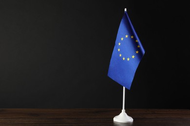 Photo of One flag of European Union on wooden table against black background. Space for text