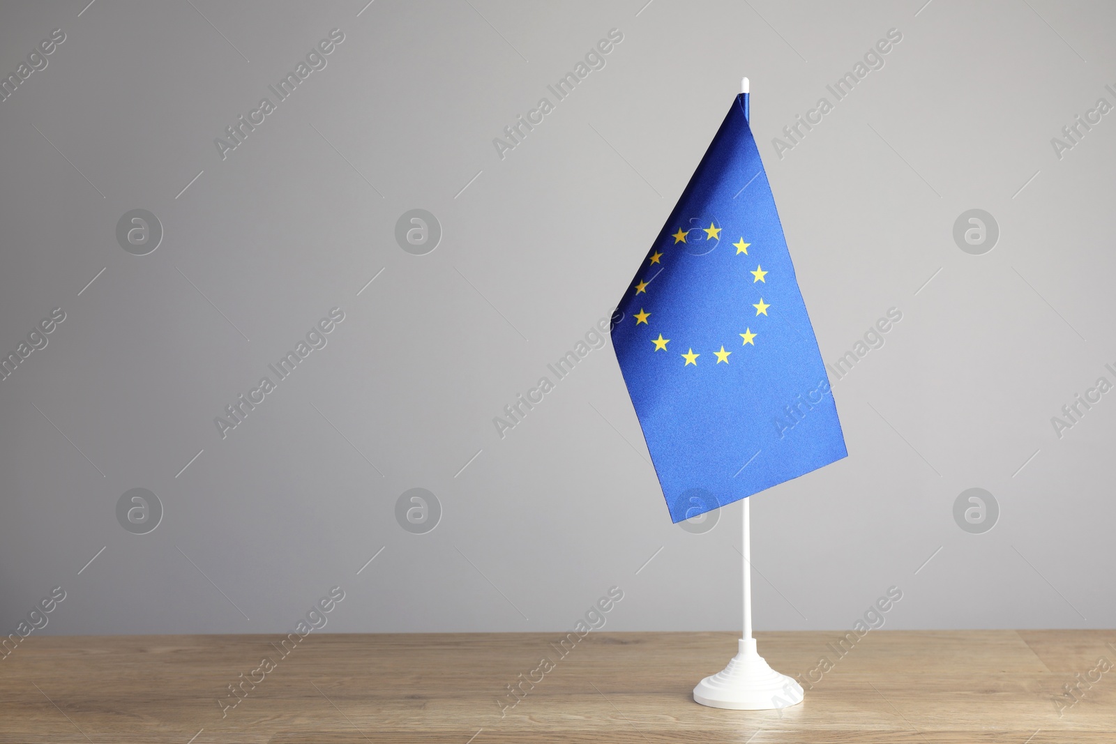 Photo of One flag of European Union on wooden table against grey background. Space for text