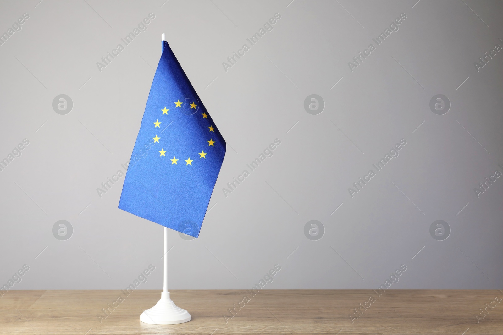 Photo of One flag of European Union on wooden table against grey background. Space for text