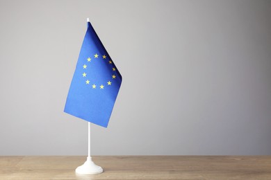 Photo of One flag of European Union on wooden table against grey background. Space for text