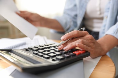 Photo of Budget planning. Woman using calculator while working with accounting document at table indoors, closeup