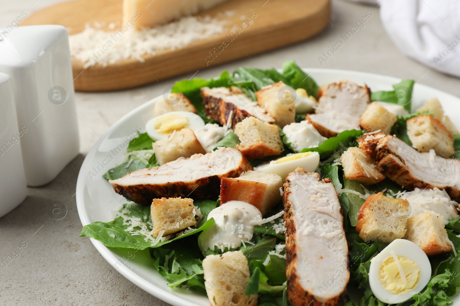 Photo of Tasty Caesar salad with chicken on light grey table, closeup