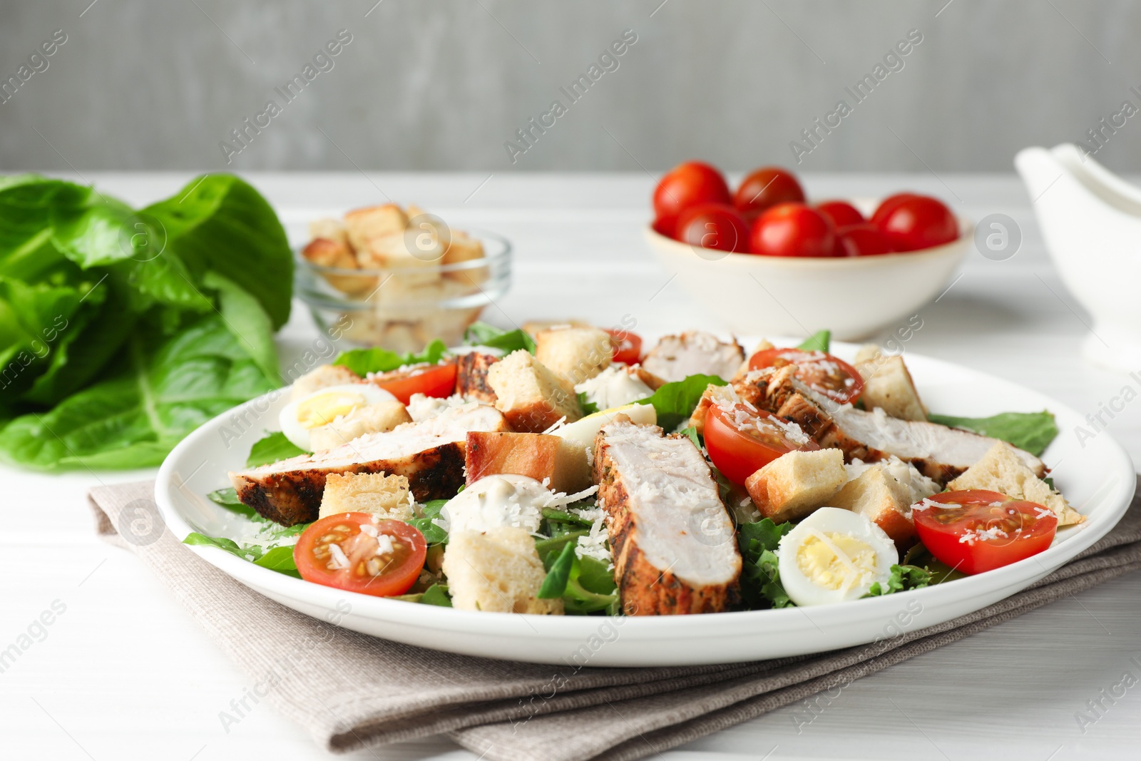 Photo of Tasty Caesar salad with chicken and tomatoes on white wooden table