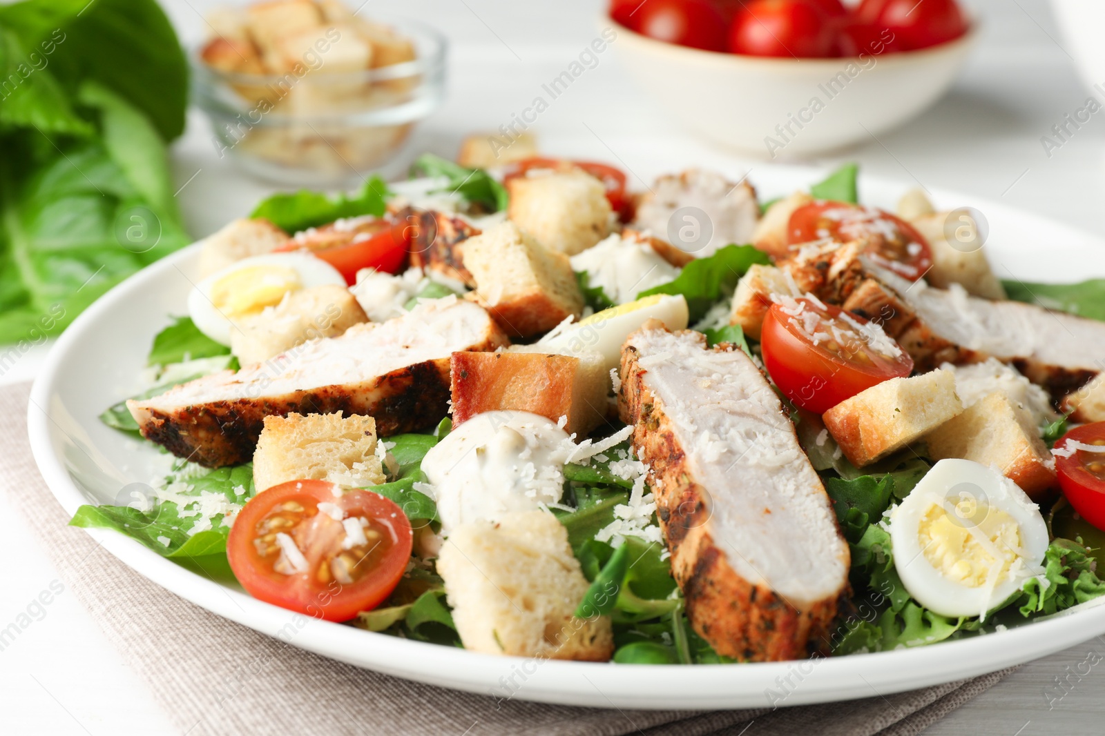 Photo of Tasty Caesar salad with chicken and tomatoes on white wooden table, closeup