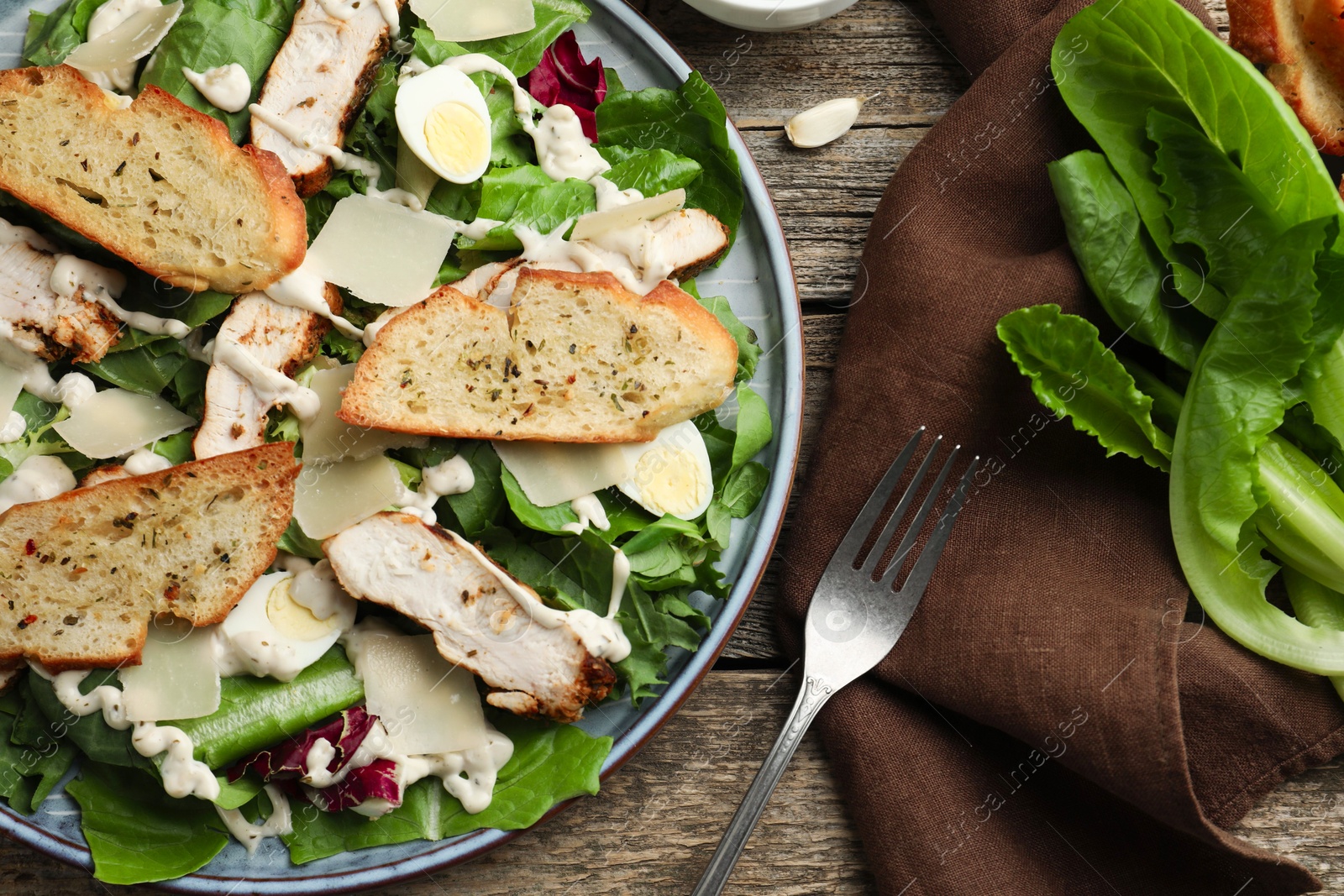 Photo of Tasty Caesar salad with chicken served on wooden table, flat lay