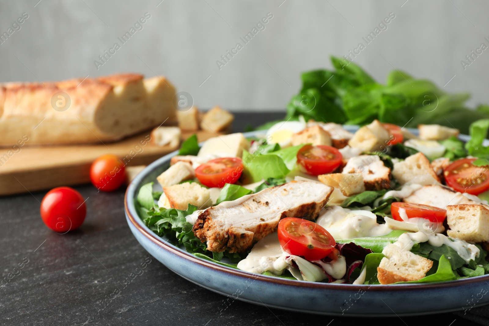 Photo of Tasty Caesar salad with chicken and tomatoes on dark gray textured table, closeup