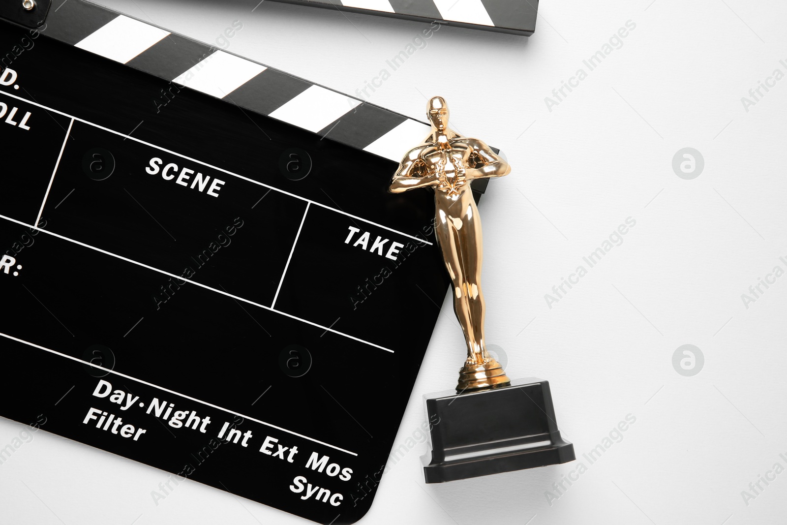 Photo of Golden trophy in shape of human figure and movie clapper on white background, top view