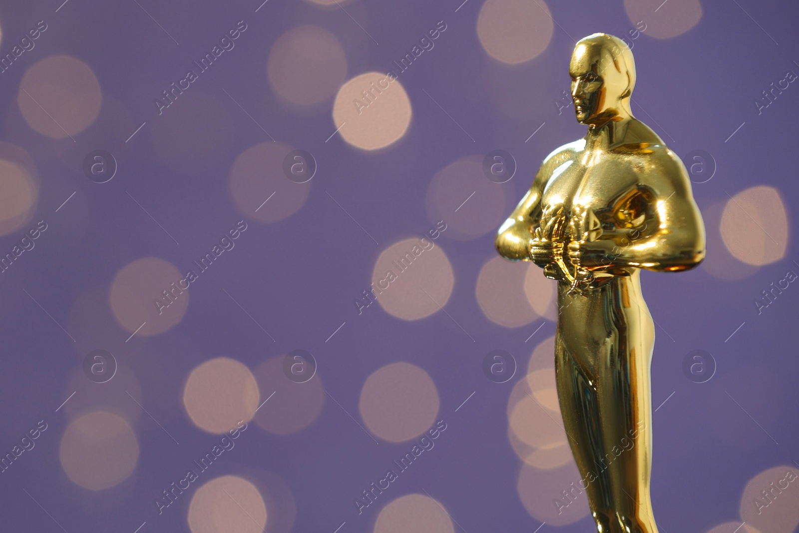 Photo of Golden trophy in shape of human figure on purple background with blurred lights, space for text