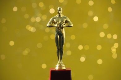 Photo of Golden trophy in shape of human figure on olive background with blurred lights