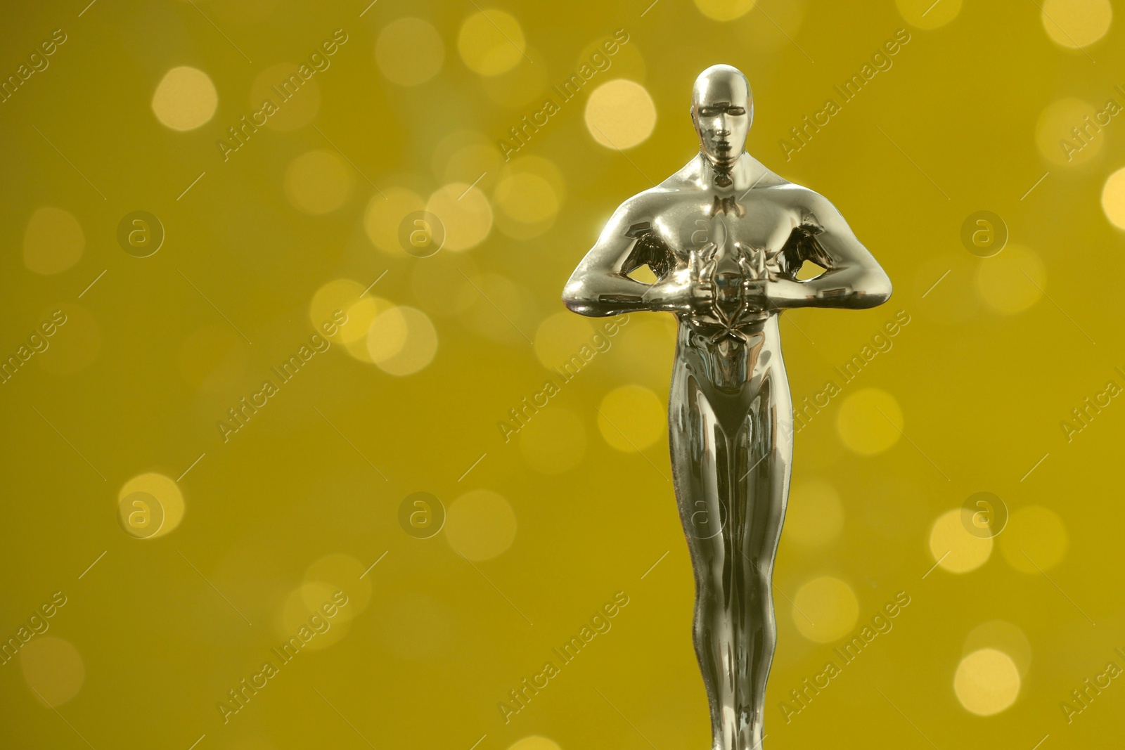 Photo of Golden trophy in shape of human figure on olive background with blurred lights, space for text