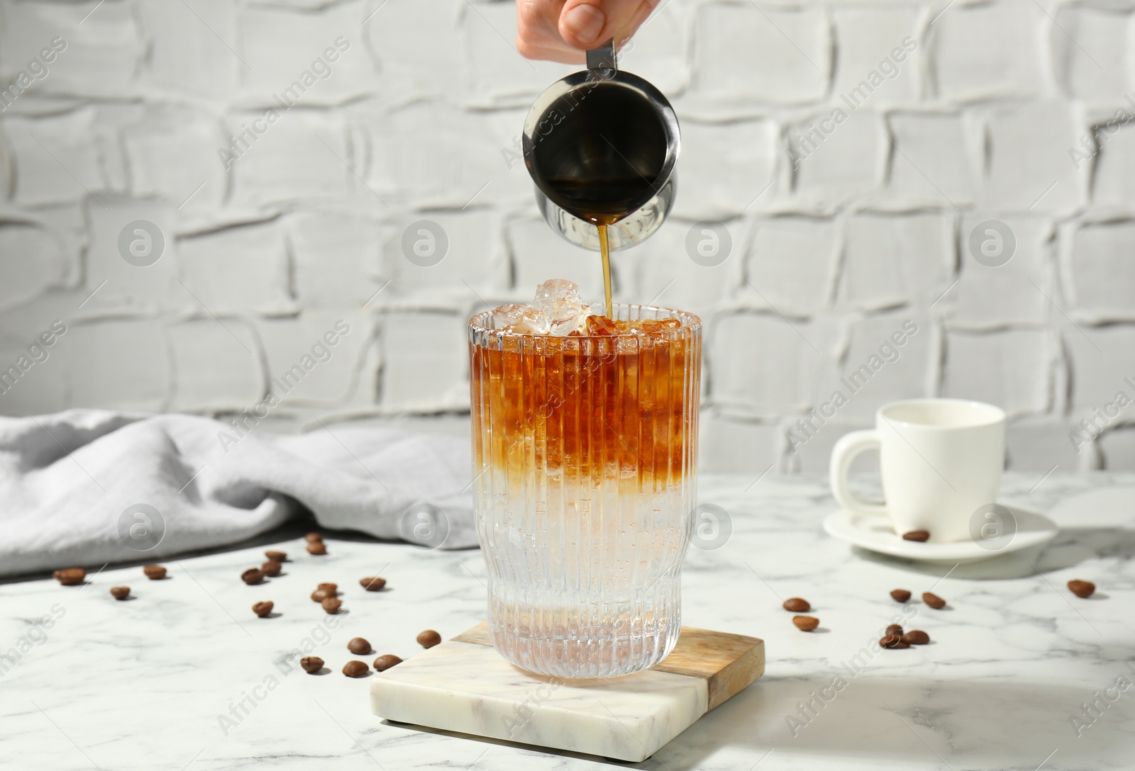 Photo of Woman making refreshing espresso tonic drink at white marble table, closeup