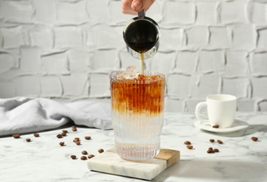 Photo of Woman making refreshing espresso tonic drink at white marble table, closeup