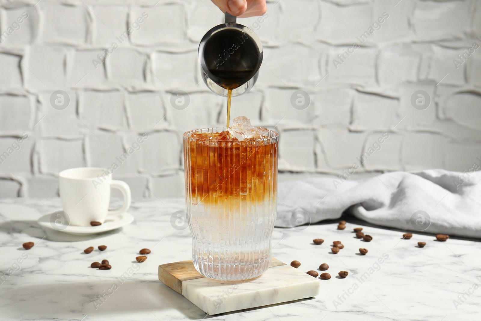 Photo of Woman making refreshing espresso tonic drink at white marble table, closeup