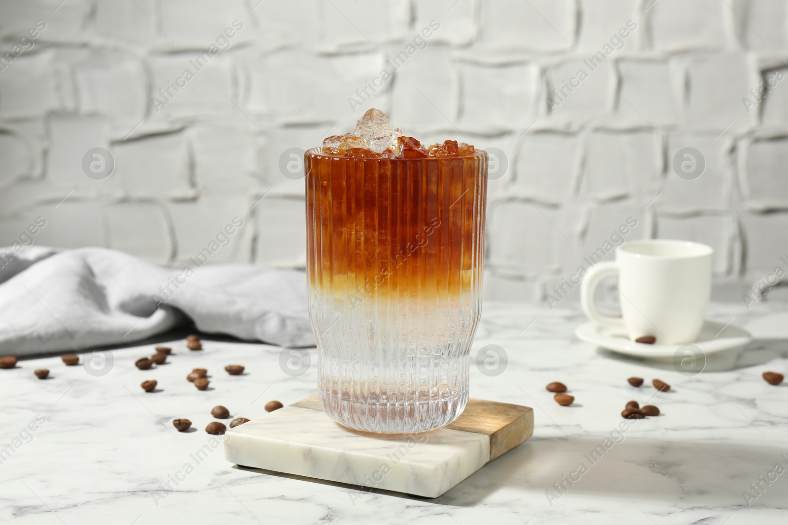 Photo of Refreshing espresso tonic drink and coffee beans on white marble table