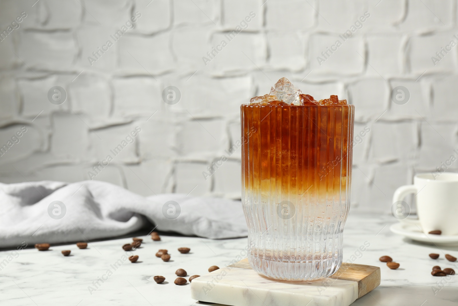 Photo of Refreshing espresso tonic drink and coffee beans on white marble table. Space for text