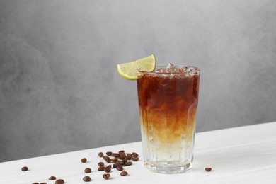 Photo of Refreshing espresso tonic drink with slice of lime and coffee beans on white wooden table