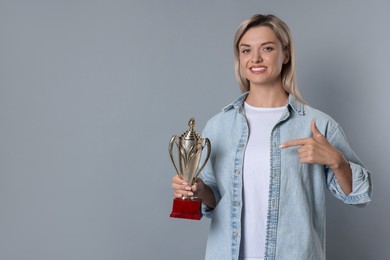 Happy winner with golden trophy cup on gray background, space for text