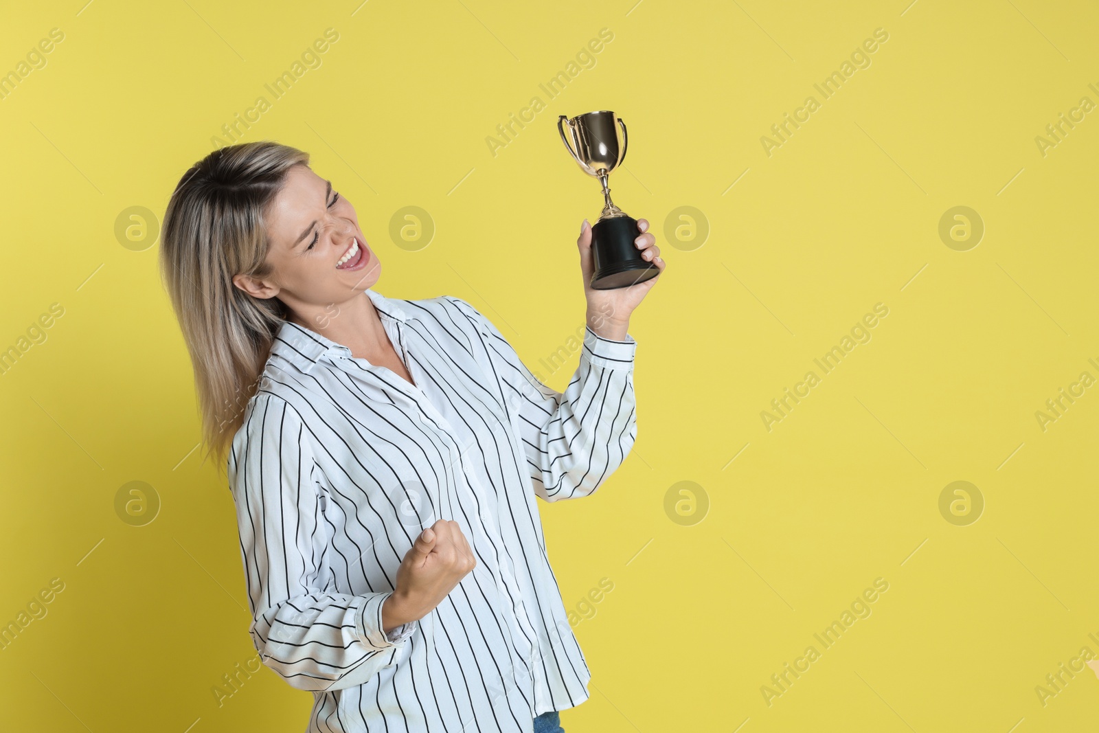 Photo of Happy winner with golden trophy cup on yellow background, space for text