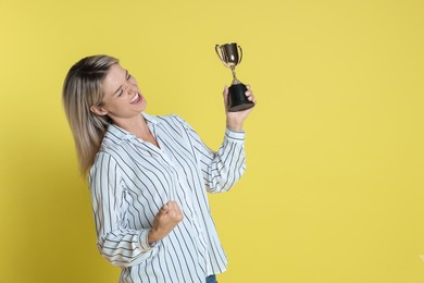 Photo of Happy winner with golden trophy cup on yellow background, space for text