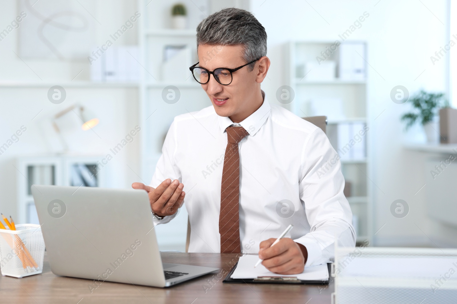 Photo of Middle aged man having videochat by laptop at table in office