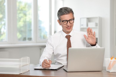 Photo of Middle aged man having videochat by laptop at table in office