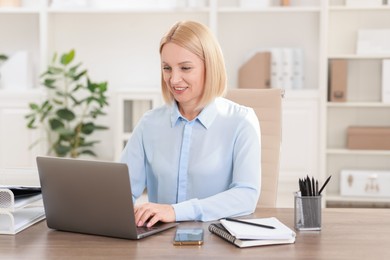 Photo of Smiling middle aged woman working with laptop at table in office