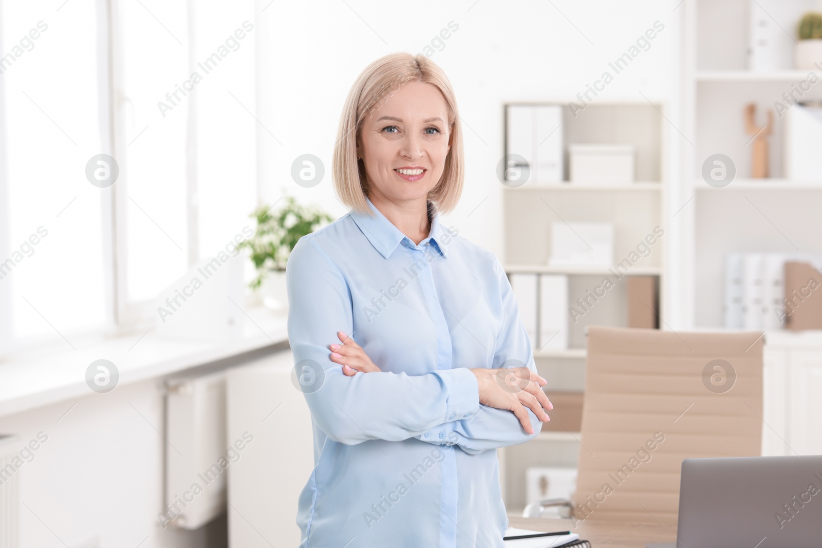 Photo of Portrait of smiling middle aged woman with crossed arms in office