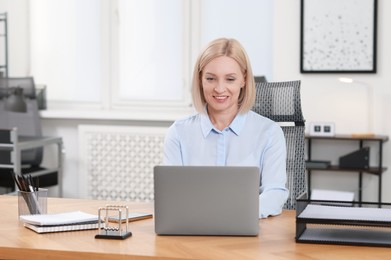 Photo of Smiling middle aged woman working with laptop at table in office