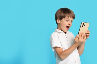 Photo of Cute little boy with smartphone on light blue background, space for text