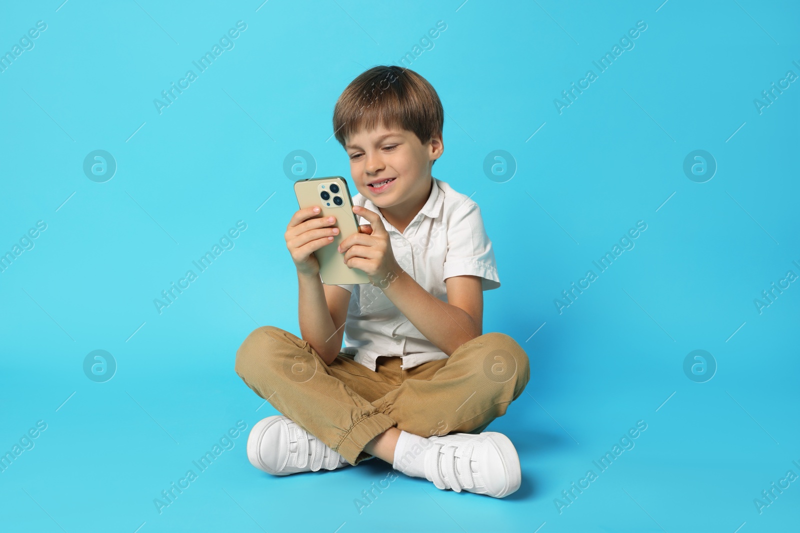 Photo of Cute little boy with smartphone on light blue background