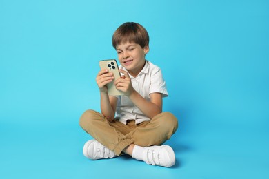 Photo of Cute little boy with smartphone on light blue background