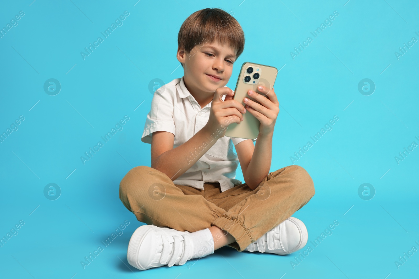 Photo of Cute little boy with smartphone on light blue background