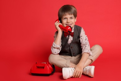 Photo of Cute little boy with old telephone on red background