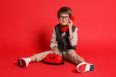 Photo of Cute little boy with old telephone on red background