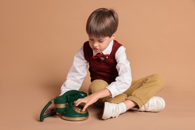 Photo of Cute little boy with old telephone on beige background