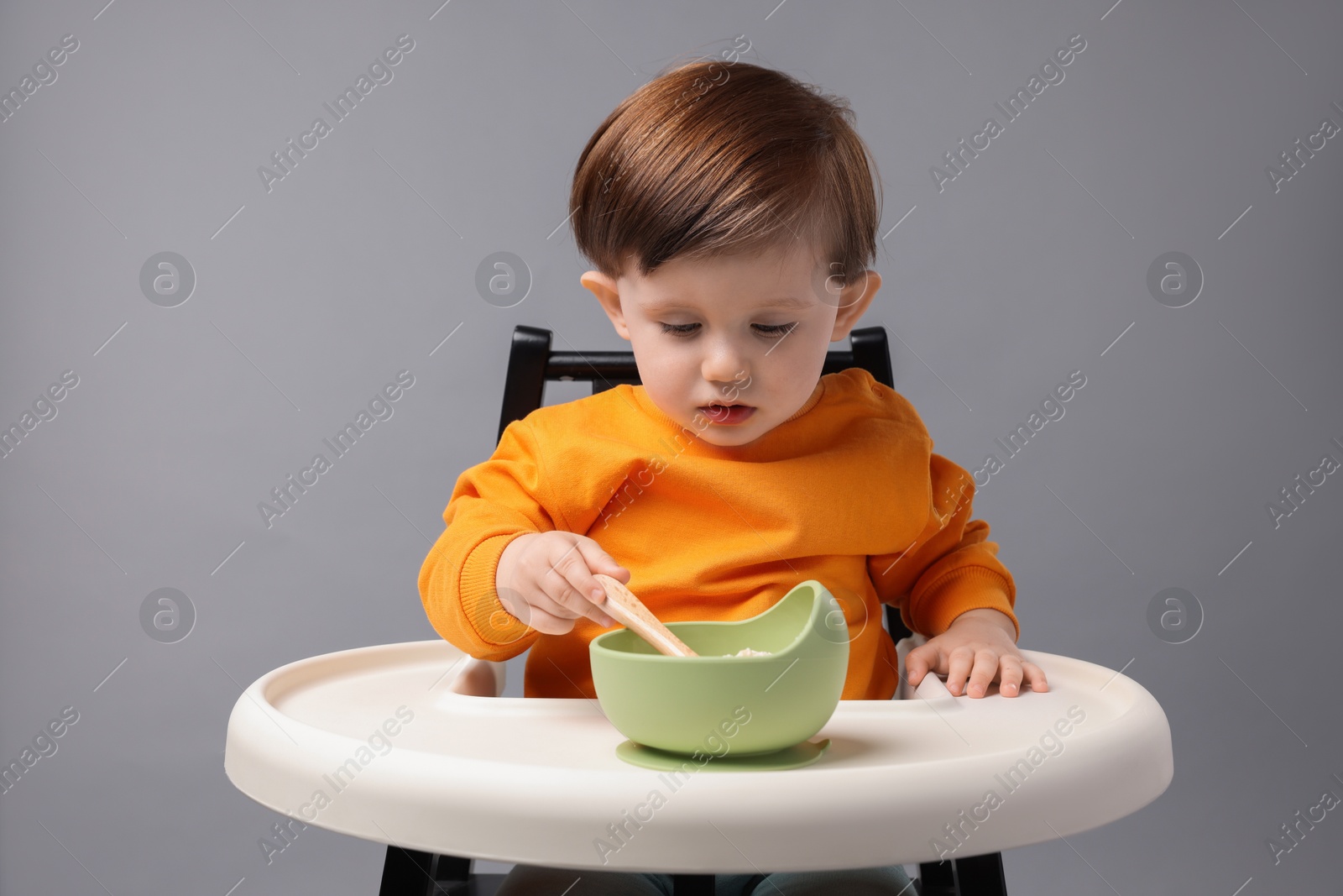 Photo of Cute little kid eating healthy baby food from bowl in high chair on light grey background