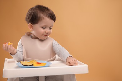 Photo of Healthy baby food. Cute little kid eating fruits in high chair on beige background, space for text