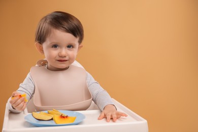 Photo of Healthy baby food. Cute little kid eating fruits in high chair on beige background, space for text