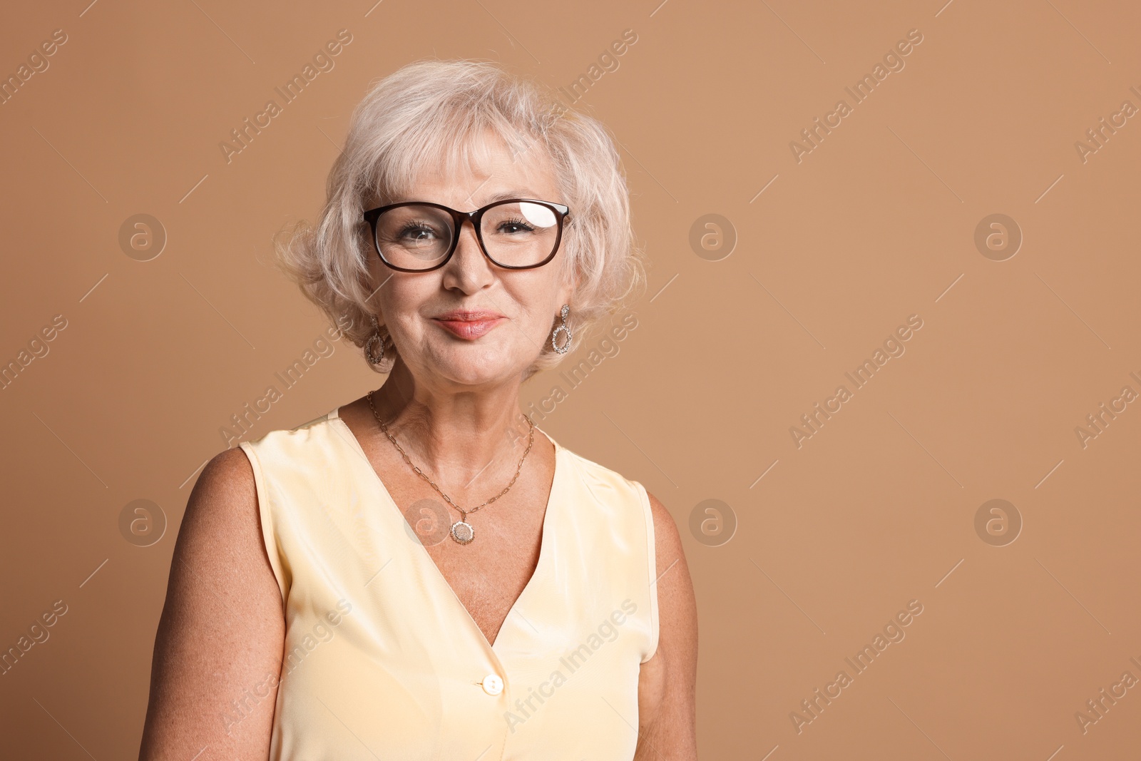 Photo of Portrait of beautiful senior woman on light brown background, space for text