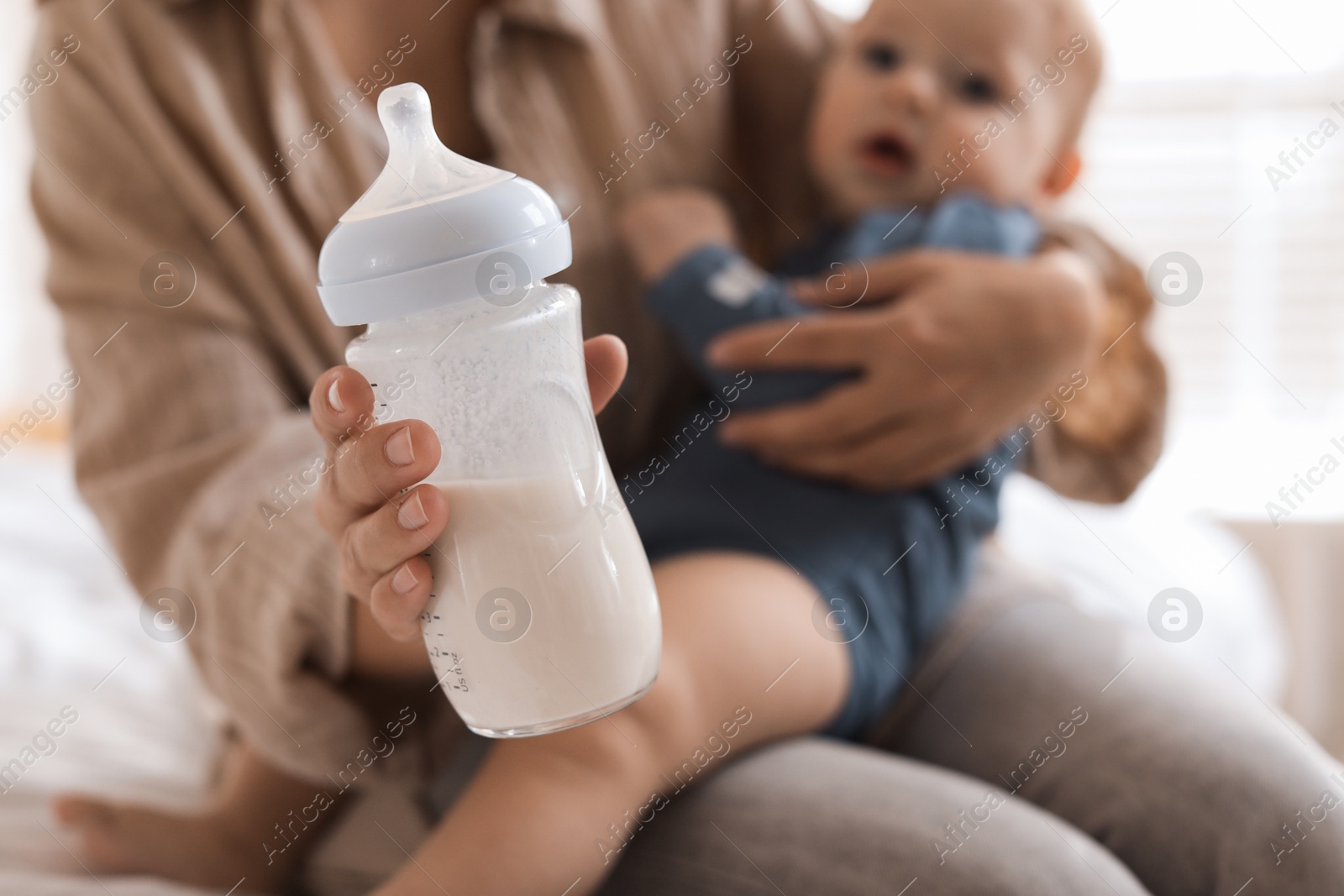 Photo of Mother holding cute little baby and bottle of milk on bed at home, selective focus