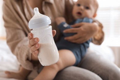 Photo of Mother holding cute little baby and bottle of milk on bed at home, selective focus