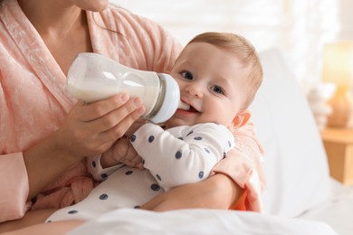 Photo of Mother feeding her little baby from bottle on bed at home, closeup