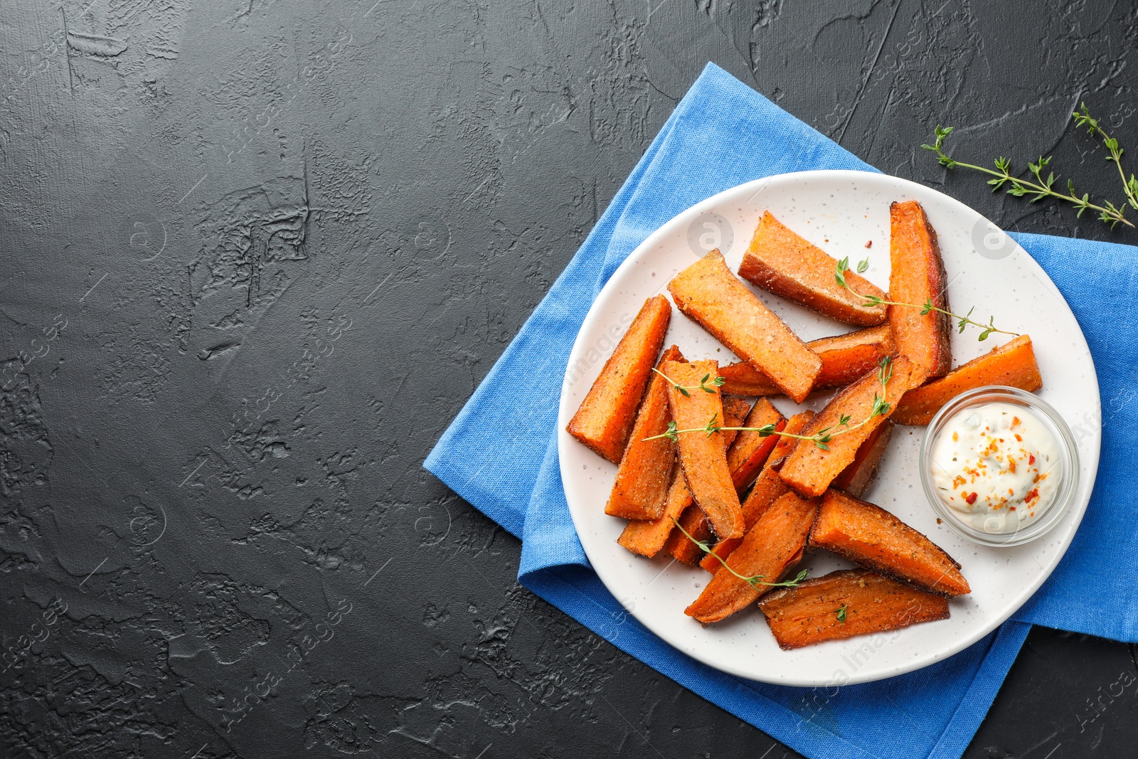 Photo of Pieces of tasty baked sweet potato with microgreens and sauce on grey textured table, top view. Space for text