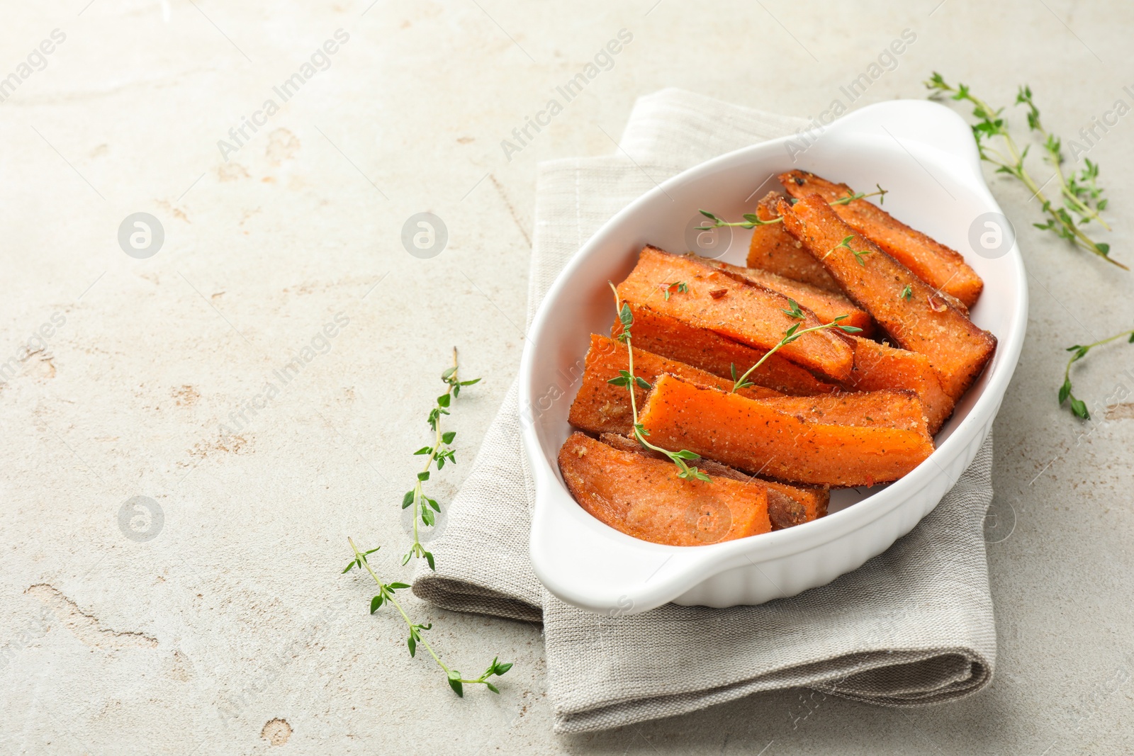 Photo of Pieces of tasty cooked sweet potato in baking dish with microgreens on light textured table. Space for text