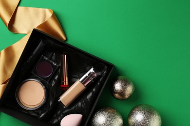 Photo of Christmas present. Decorative cosmetics in gift box and festive balls on green background, flat lay