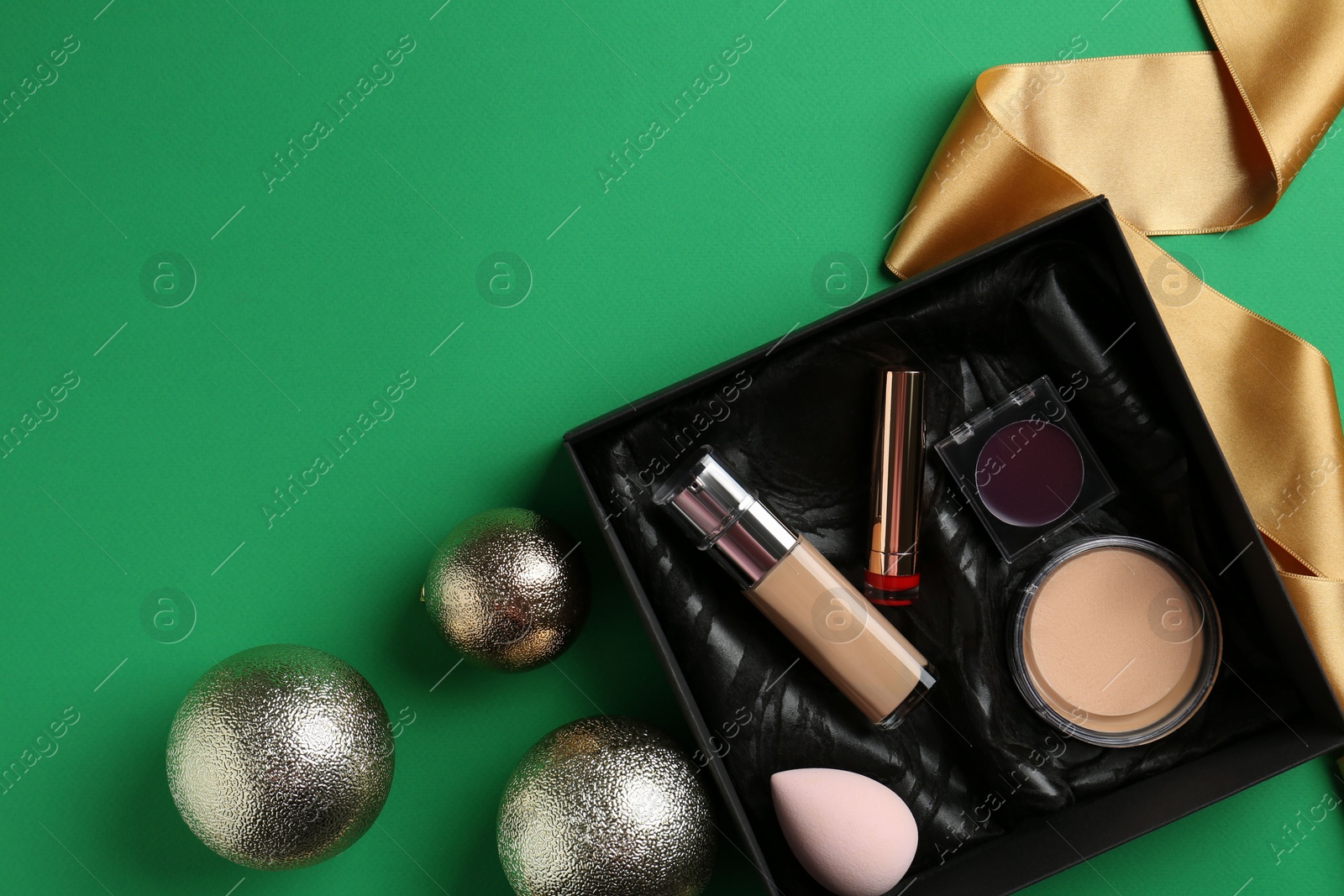 Photo of Christmas present. Decorative cosmetics in gift box and festive balls on green background, flat lay